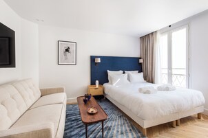 A hotel room with a bed, a sofa, a nightstand, and a window with curtains.