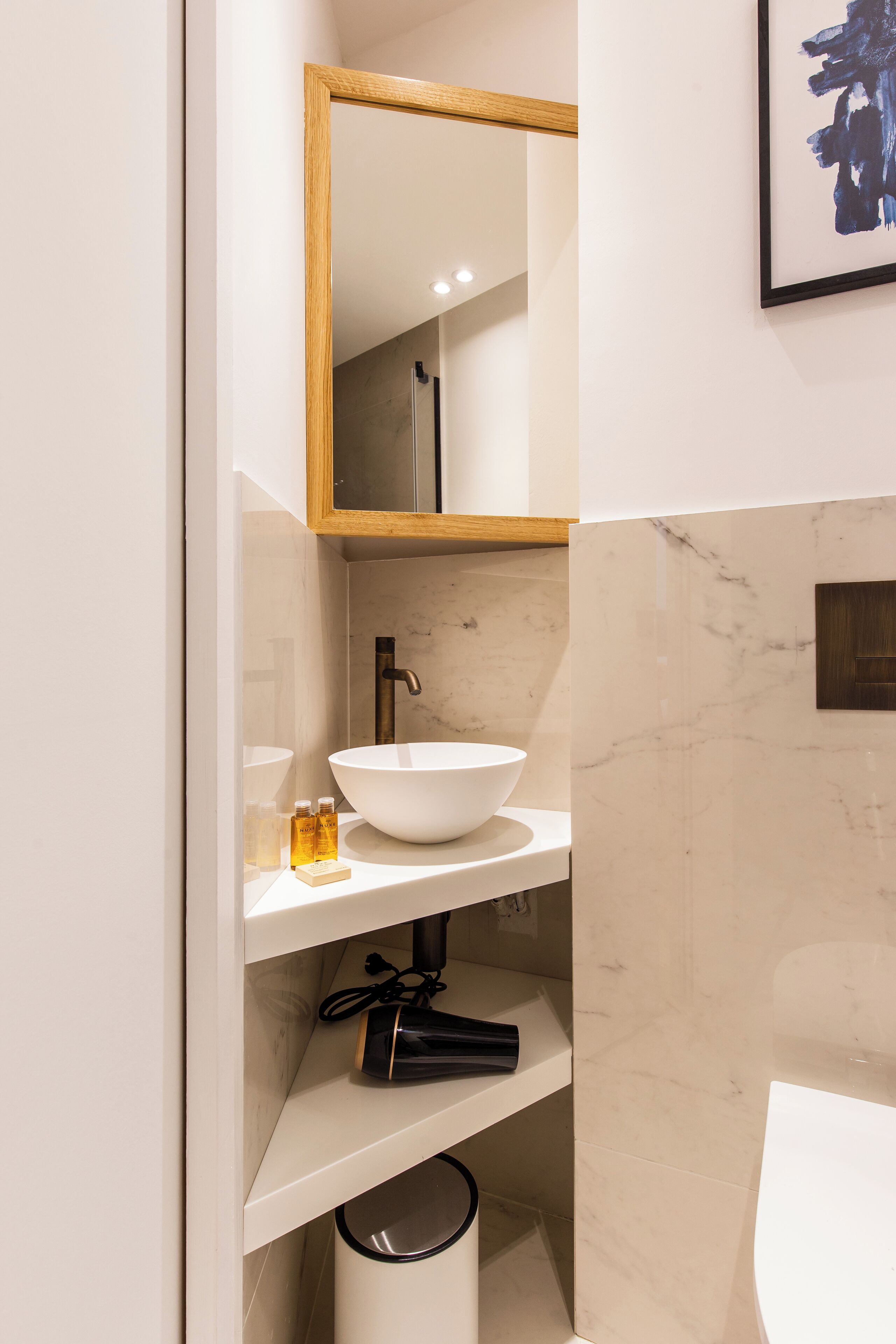 Un baño con lavamanos blanco, espejo y pared de mármol.