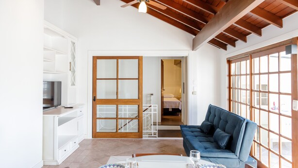 A spacious living area with a blue sofa, a dining table set with plates and glasses, and a television on a cabinet. - LOCAR-IN GRAMADO- Leonardo da Vinci (Gramado)