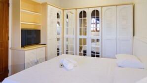 A hotel room with a large bed, white bedding, a television on a stand, and a wardrobe with multiple doors. - LOCAR-IN GRAMADO- Leonardo da Vinci (Gramado)