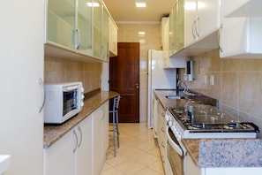 A kitchen with white cabinets, a microwave, a gas stove, and a refrigerator.