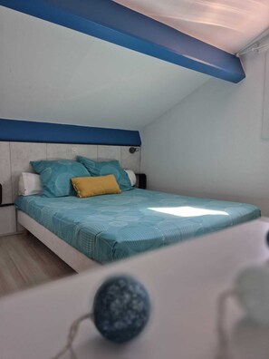 Une chambre avec un plafond en pente, un lit recouvert d’une couvre-lit à motifs et une table de chevet.