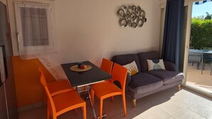 A living room with a sofa, a dining table with chairs, a hanging light fixture, and a decorative wall piece.