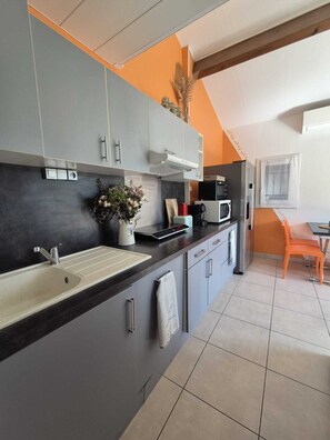 A modern kitchen with grey cabinets, a black countertop, and a white sink. There is a potted plant on the counter and a microwave oven.