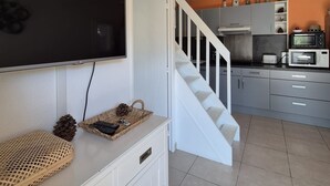 A modern kitchen with a white staircase, a flat-screen TV mounted on the wall, and a microwave on the countertop.