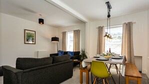 A modern living room with a sofa, dining table, and chairs. - Saint James By The Quay (Ilfracombe)
