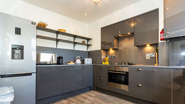 A modern kitchen with stainless steel appliances, wooden flooring, and built-in shelves. - Saint James By The Quay (Ilfracombe)