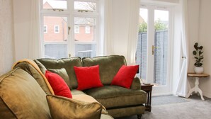 A green sofa with red cushions in a room with a white door and a small wooden table. - Pippin's Place (Shrewsbury)