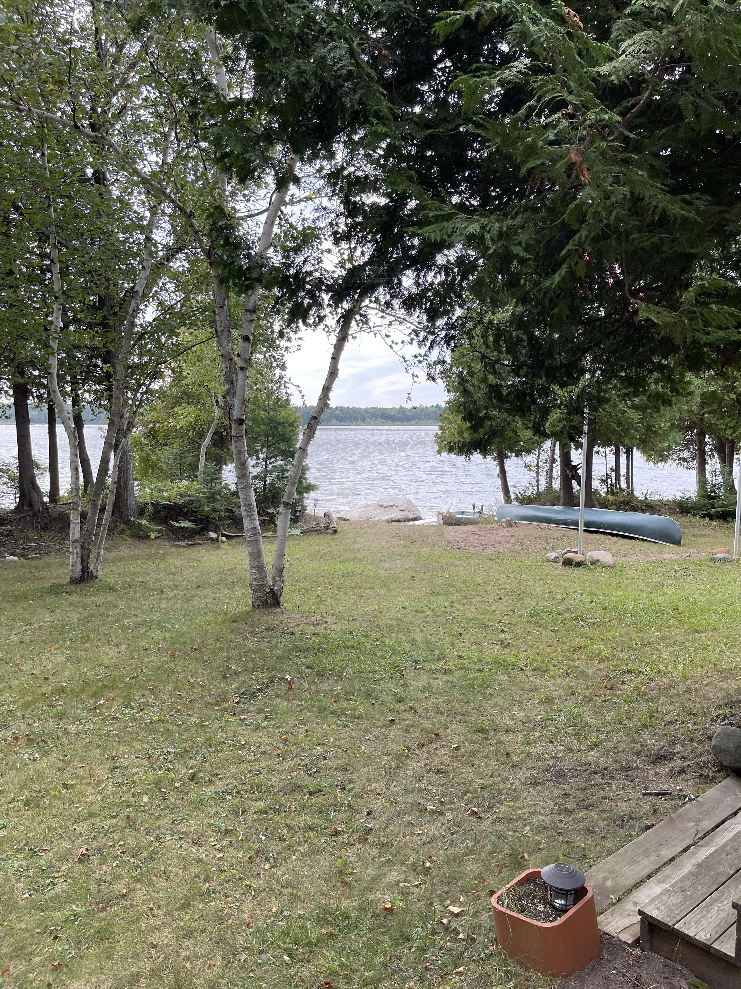 Een gazon met bomen, een houten terras en een kano aan het water.