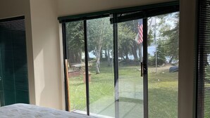 Ein Schlafzimmer mit einem großen Bett, einer Schiebetür zum Garten und Blick auf Bäume und eine Flagge.