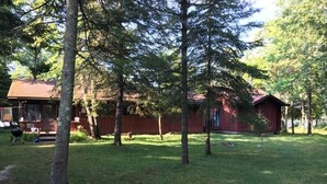Eine rote Holzhütte mit eingezäuntem Grundstück, umgeben von Bäumen.