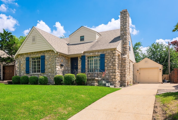 A stone house with a chimney, a garage, and a well-maintained lawn.