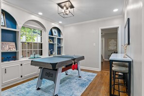 A room with a pool table, shelves with framed pictures, and a bar stool.