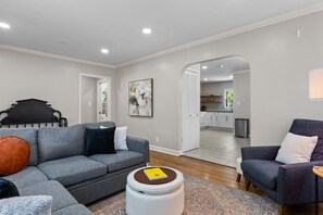A modern living room with a gray sofa, a round ottoman, and a purple armchair.