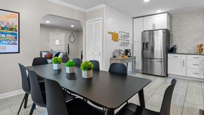 A modern kitchen with a stainless steel refrigerator, white cabinetry, and a dining area with a dark table and black chairs.