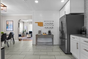 A modern kitchen with a refrigerator, coffee maker, and a dining area with chairs and a table.