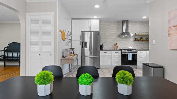 A modern kitchen with stainless steel appliances, a dining area with a black table and chairs, and a white door with louvered shutters.