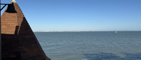 A view from a balcony overlooking a calm sea with a distant city skyline.