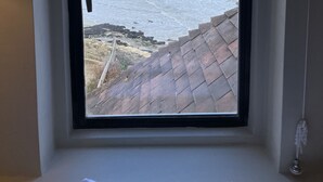 Een kamer met een raam dat uitkijkt op een wateroppervlak en een verre stadshemel.