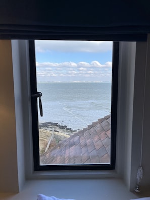 Een kamer met een raam dat uitkijkt op een wateroppervlak en een verre stadshemel.