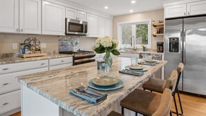 A modern kitchen with white cabinets, stainless steel appliances, a marble countertop, and a central island with a vase of flowers.