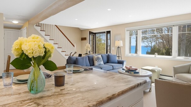 A modern living room with a marble coffee table, a blue sofa, and a view of the sea through large windows.