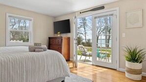 A bedroom with a bed, a dresser, a TV, and a sliding glass door leading to a patio with outdoor furniture.