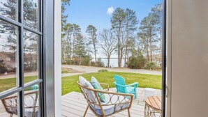 A deck with wicker chairs and a small table, overlooking a grassy area and trees.