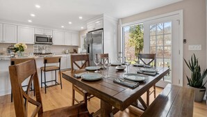 A modern kitchen with white cabinets, stainless steel appliances, and a wooden dining table set for six.