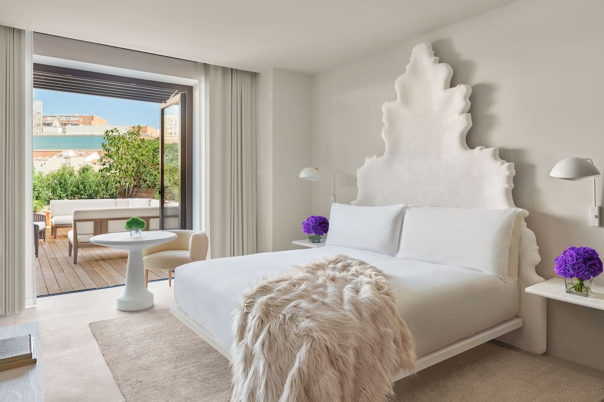 A modern hotel room with a large bed, a round table, and a view of the city through the balcony.