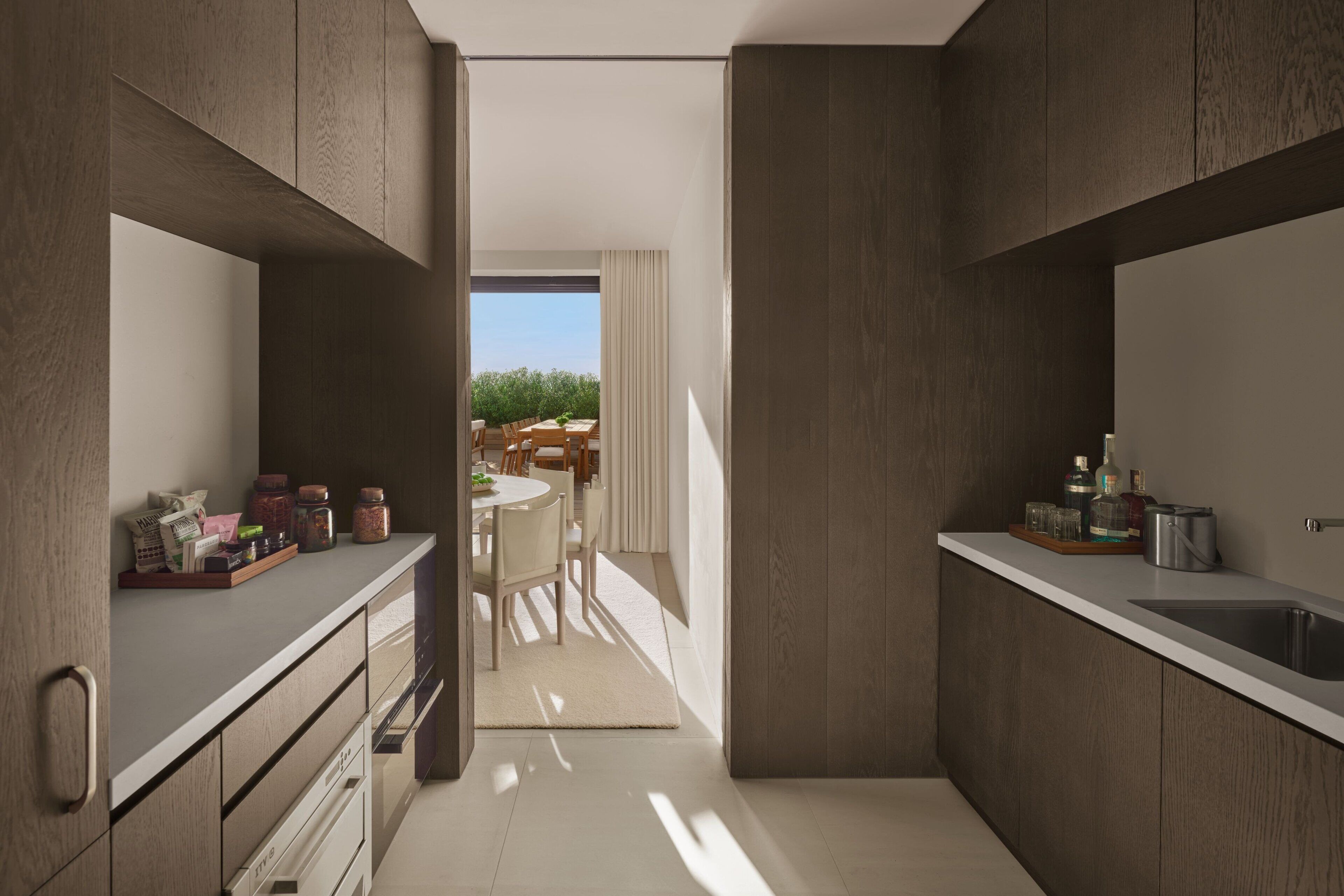 A modern kitchen with wooden cabinets, a white countertop, and a view to a dining area.