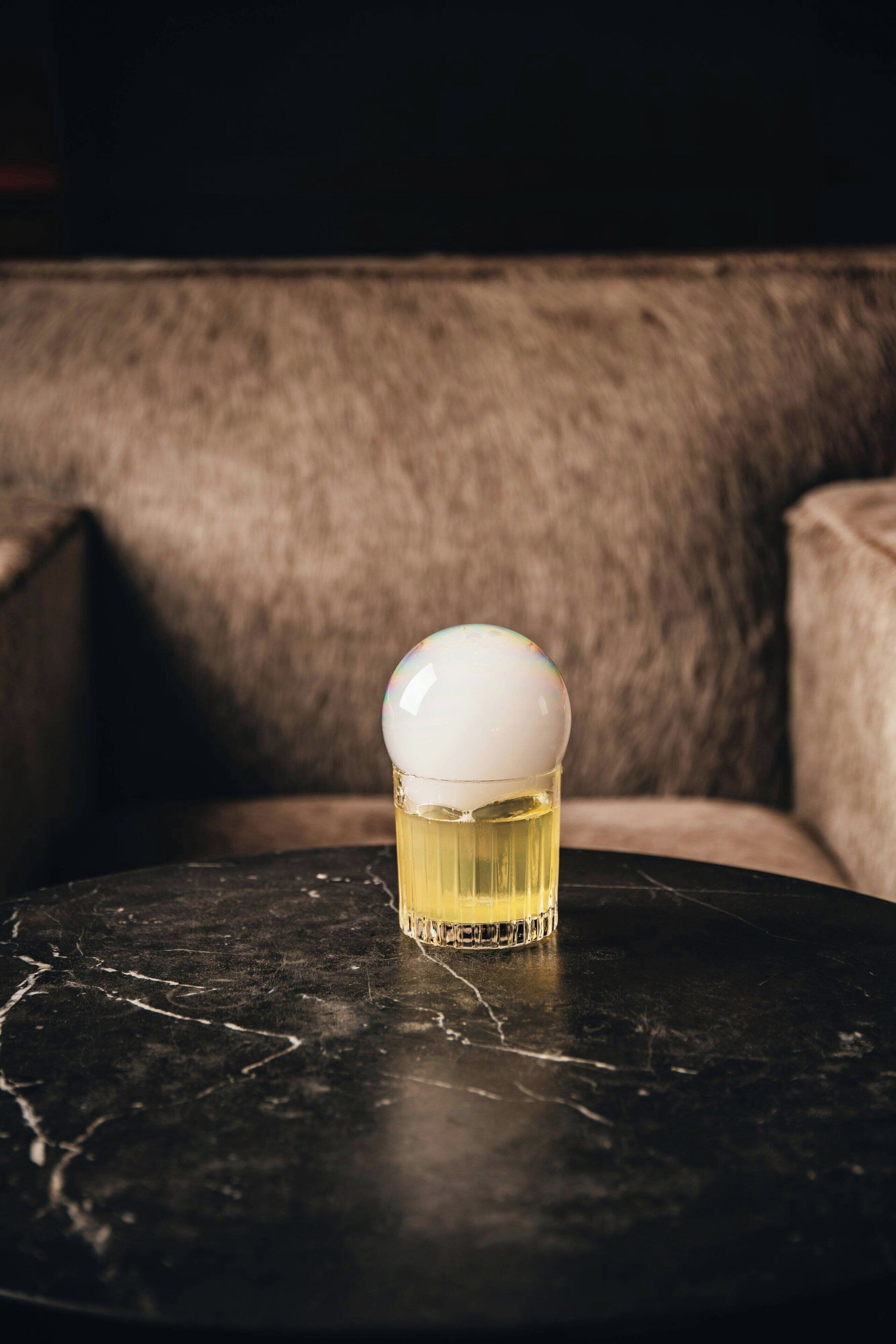 A round table with a glass containing a yellow liquid, set on a dark marble surface.