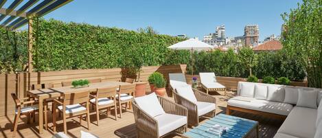 An outdoor patio with wooden furniture, a blue table, and a white umbrella.