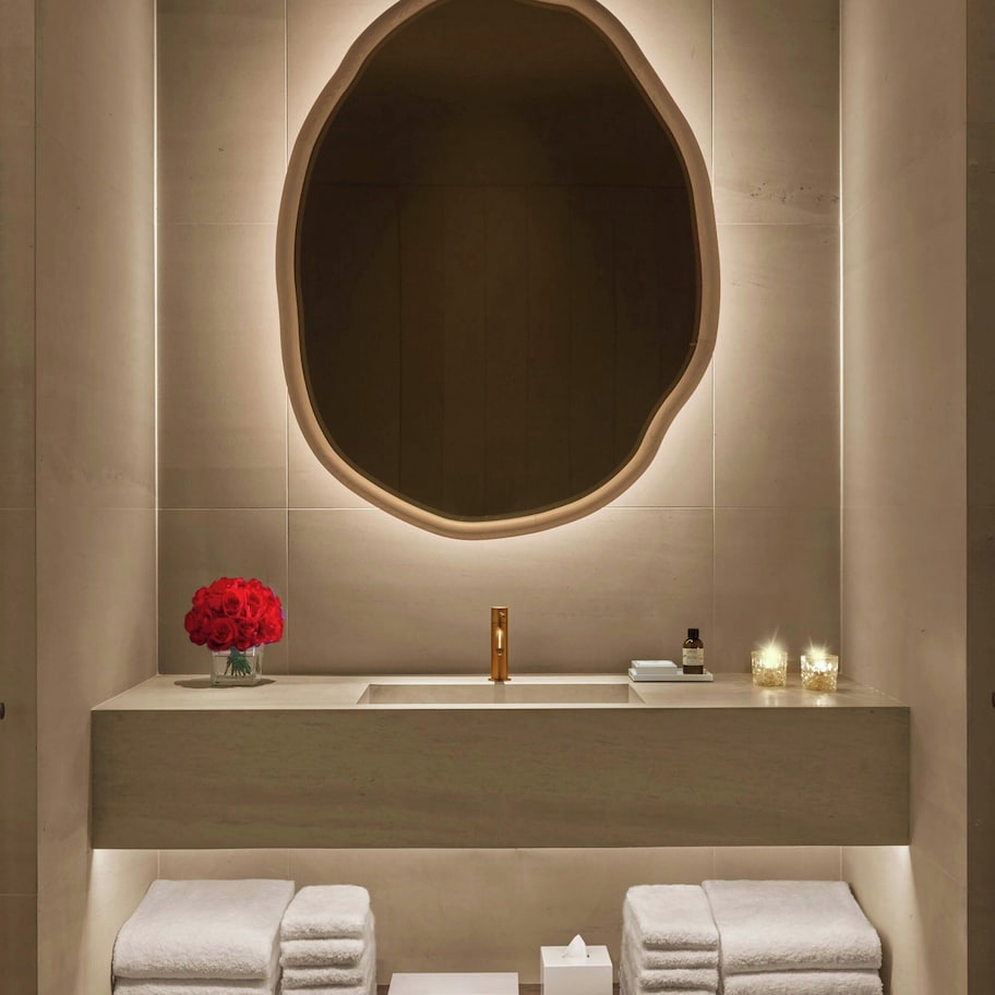 A modern bathroom with a large oval mirror, a sink, and a shelf with towels and toiletries.