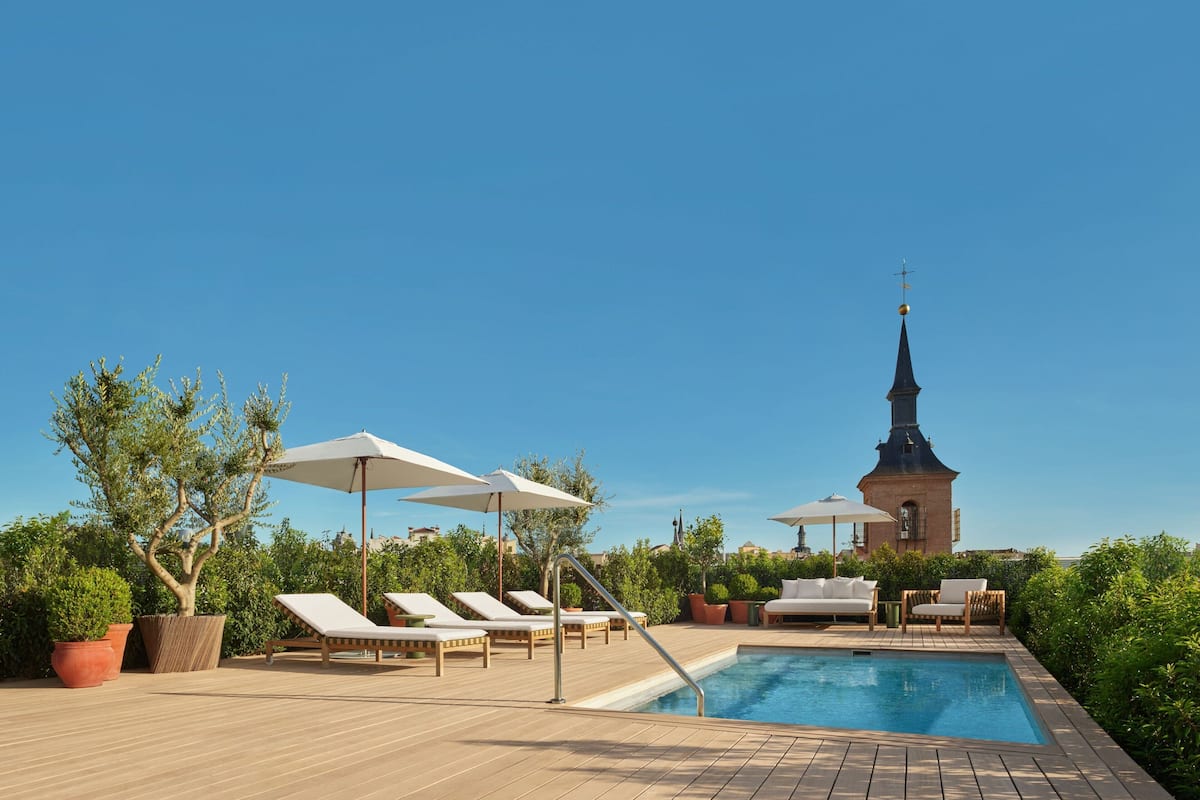 A poolside area with lounge chairs, umbrellas, and potted plants.