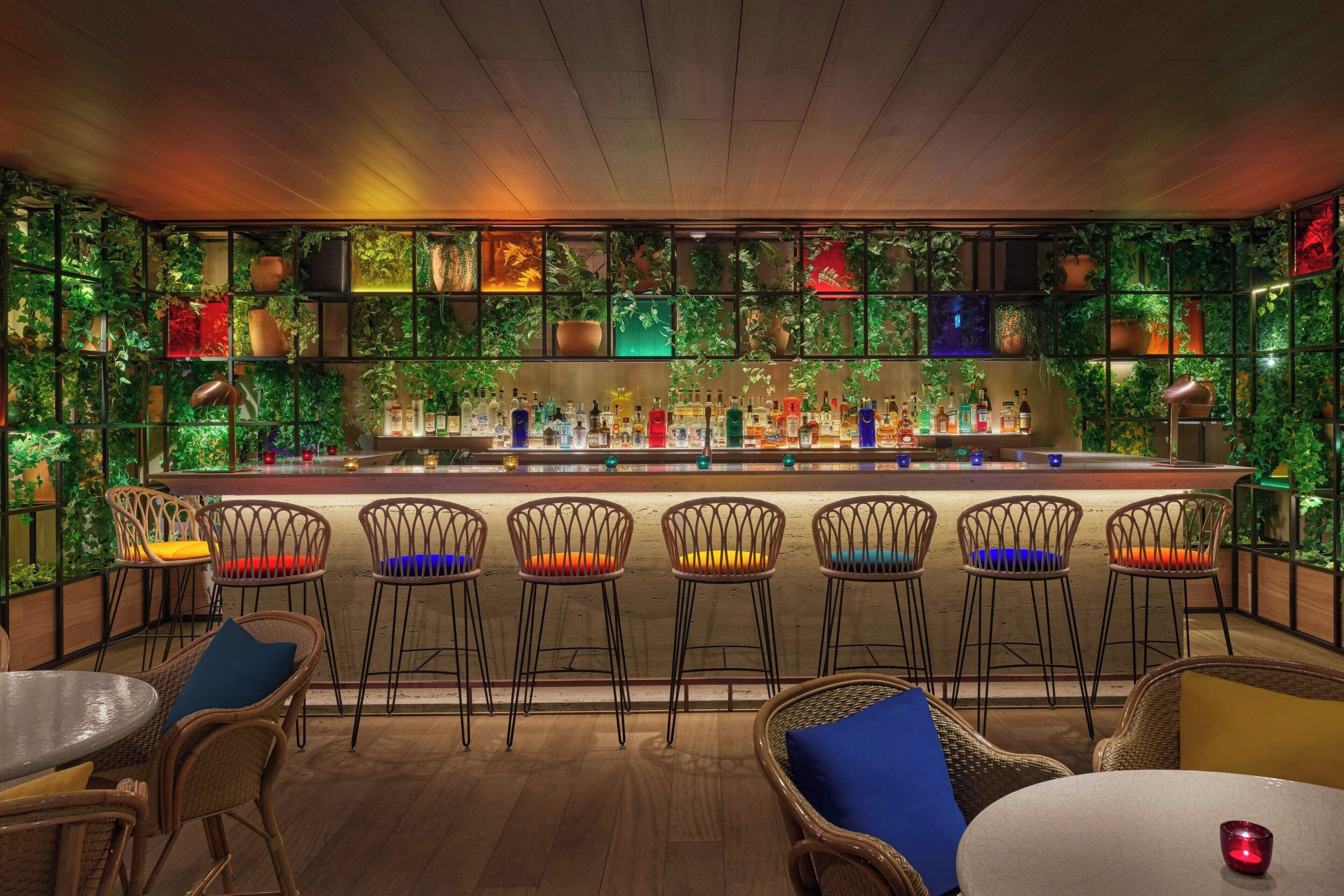 A bar area with a wooden ceiling, green plants on the walls, and a variety of bar stools and tables.
