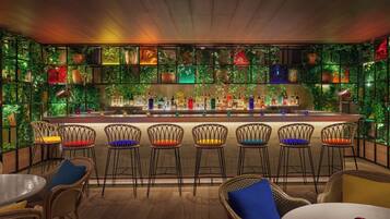 A bar area with a wooden ceiling, green plants on the walls, and a variety of bar stools and tables.