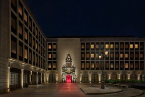 En byggnadsfasad i nattljus, med upplysta fönster och en central entré som har en rödmarkerad valvöppning.