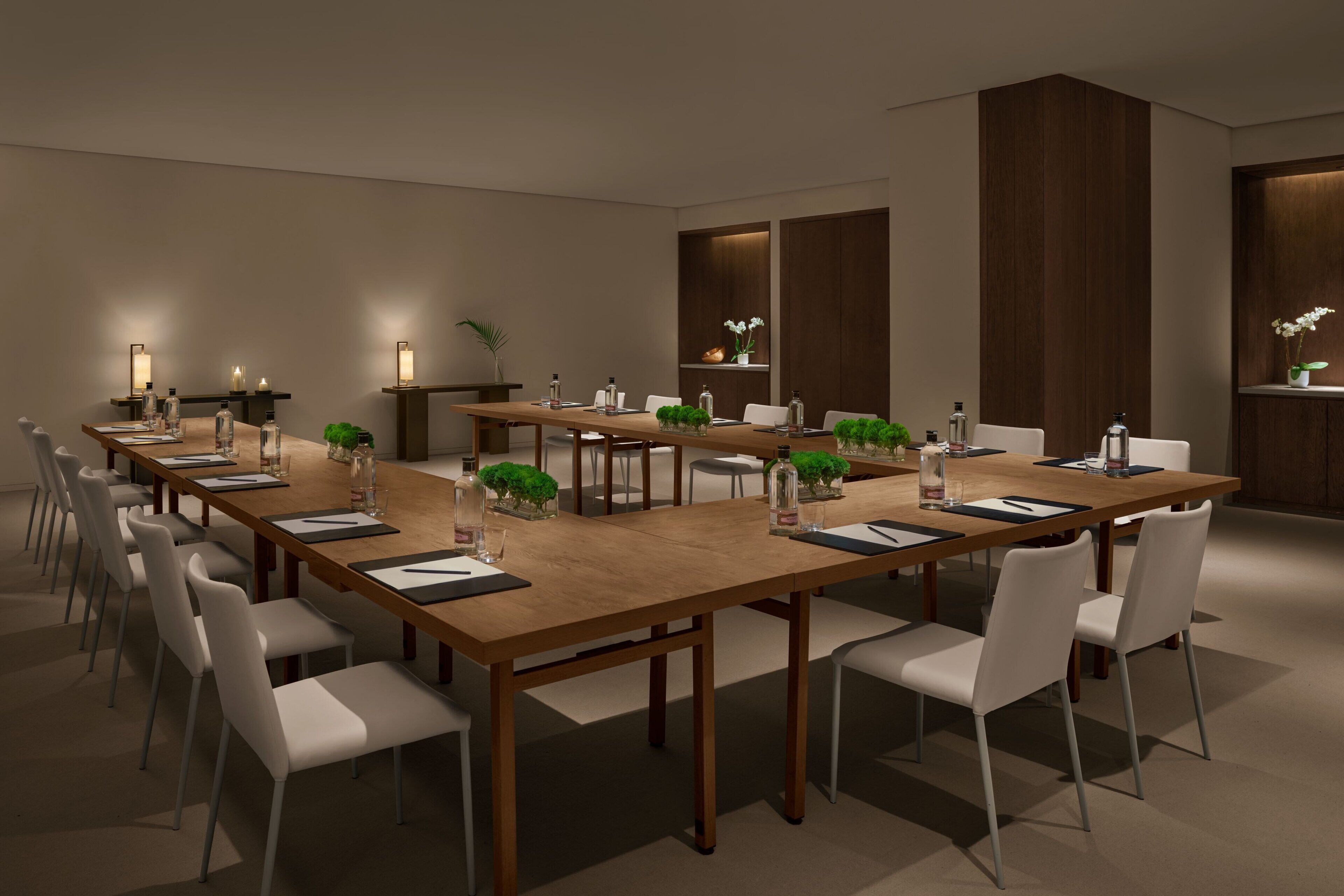 A modern conference room with a long wooden table, white chairs, and small potted plants.