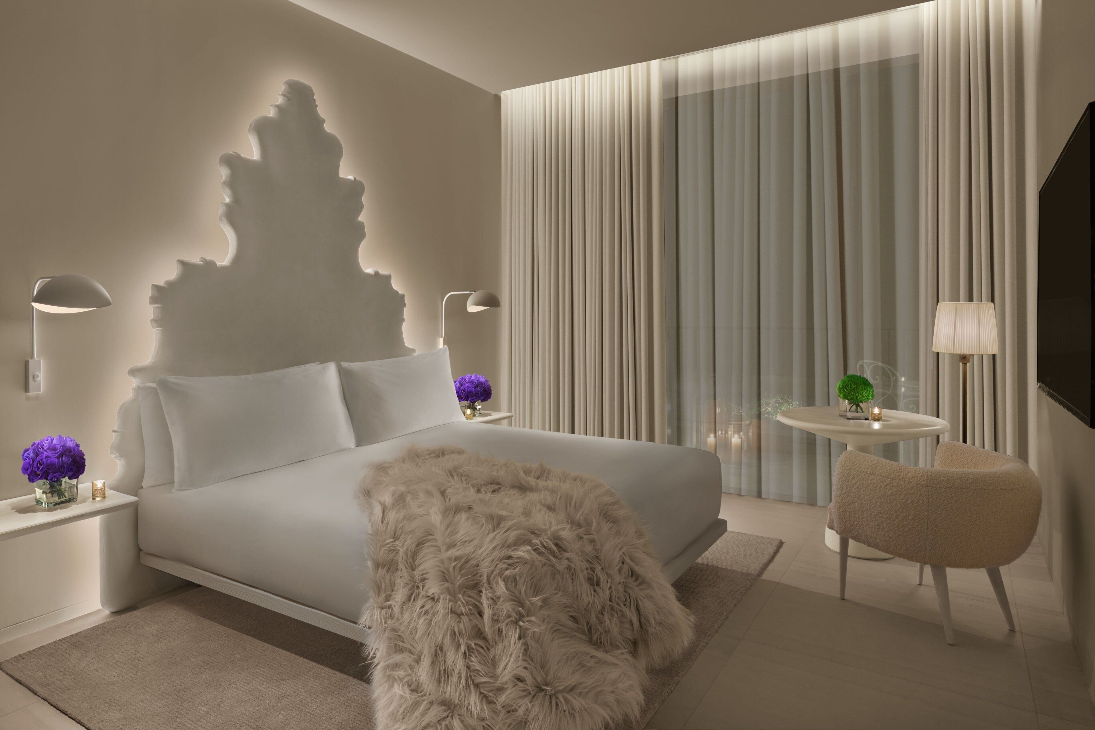 Une chambre à coucher moderne avec un lit, des tables de chevet, un tapis moelleux, une chaise et une table avec une lampe.