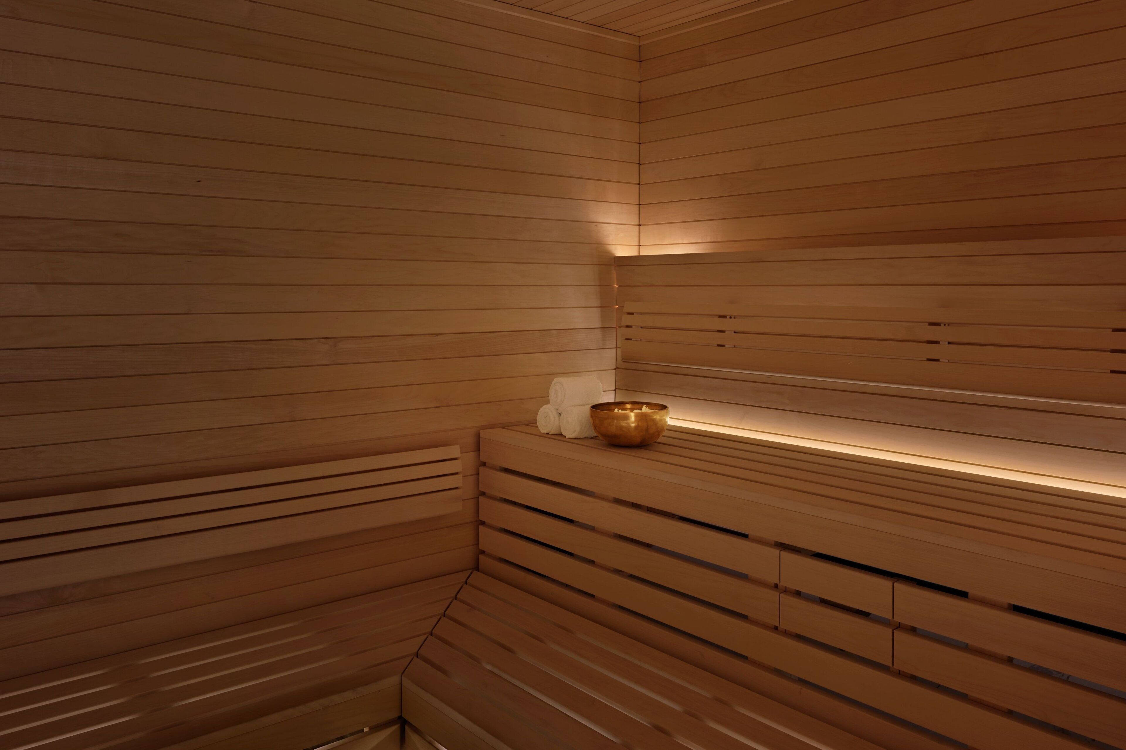 A wooden sauna with benches and a shelf holding towels and a bowl.