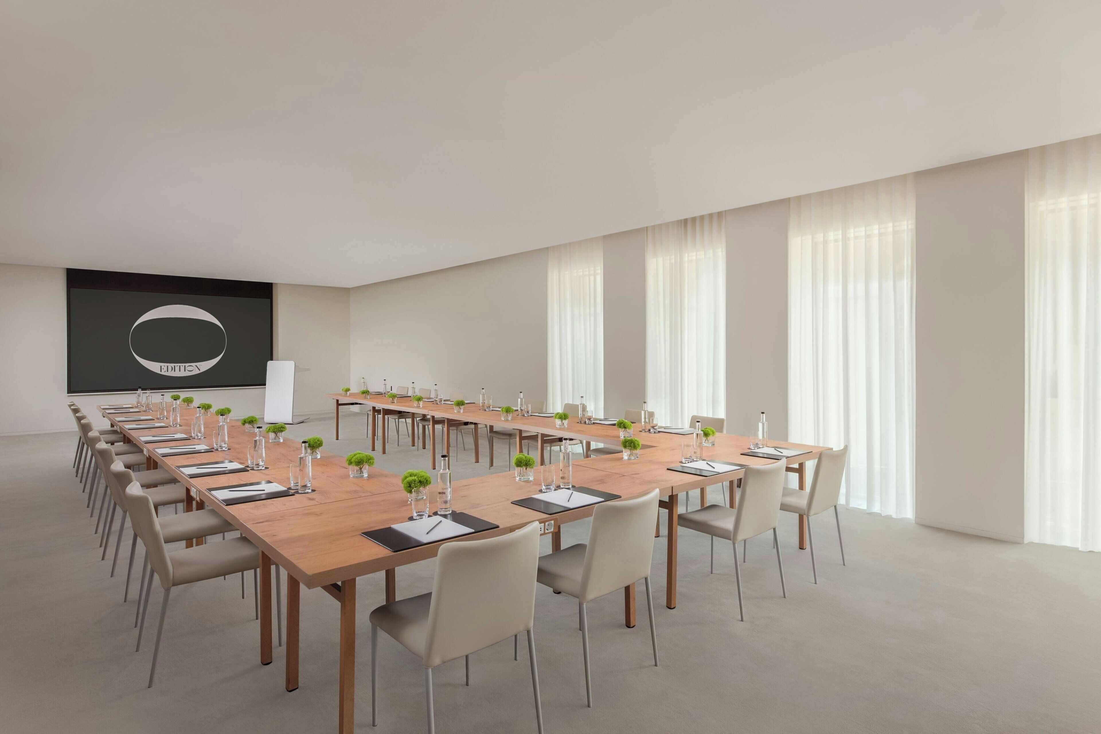 Una sala de conferències amb una taula llarga, cadires i una pantalla de projector.
