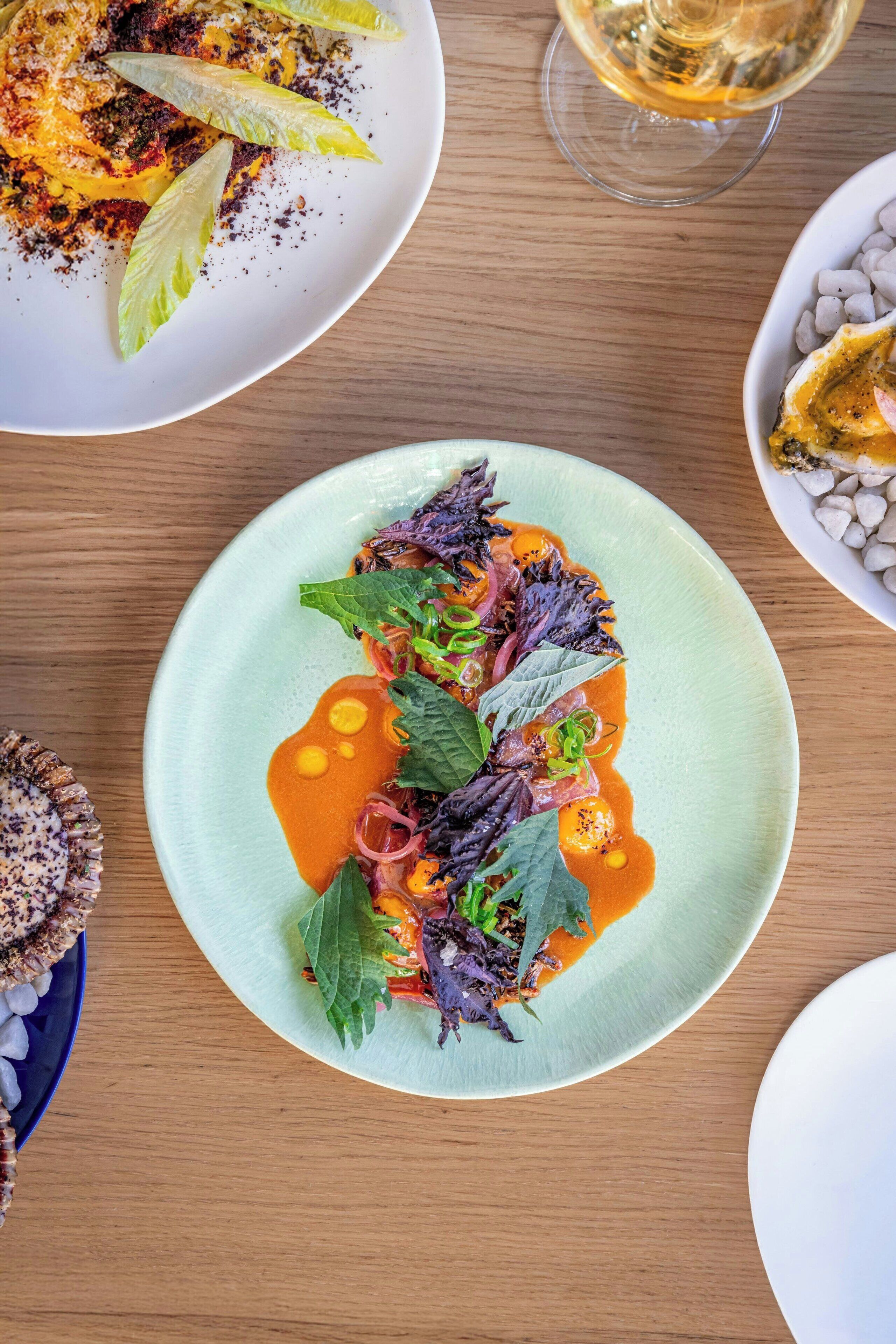 A dining table with various plates of food, including a green plate with a salad and a white plate with a dessert.