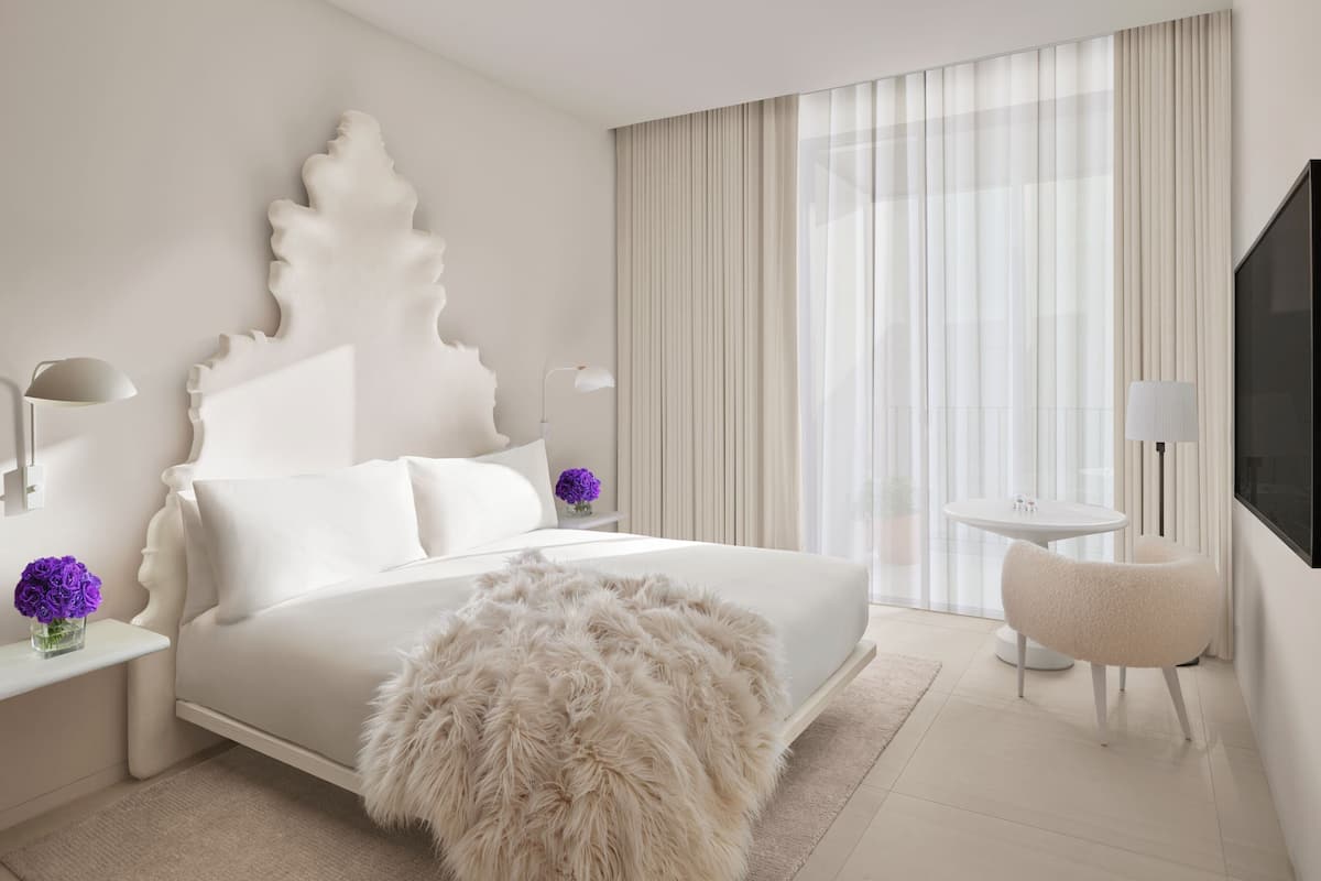 A modern hotel room with a large bed, a fluffy rug, a round table with chairs, and a TV mounted on the wall.