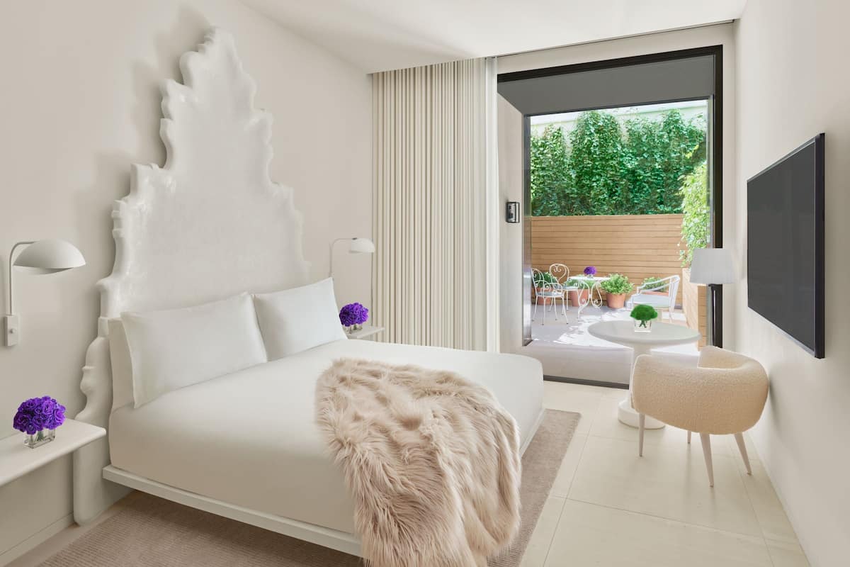 A modern bedroom with a large bed, a fluffy throw, a small round table, and a chair.