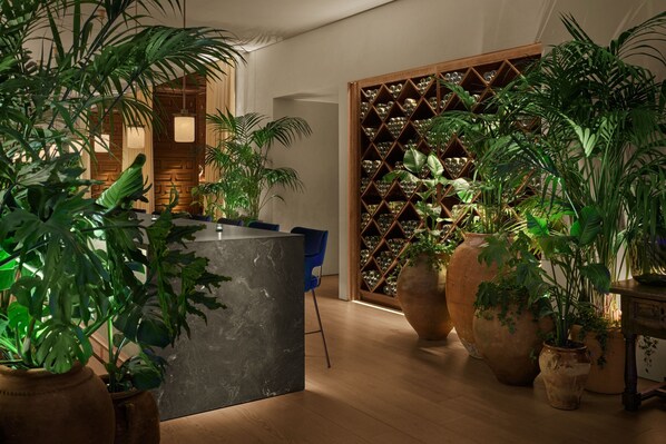 A modern interior with a central reception desk, large potted plants, and a wine rack in the background. - The Madrid EDITION (Madrid)