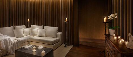 A modern living room with a sectional sofa, a dark marble coffee table, and a wooden cabinet with candles.