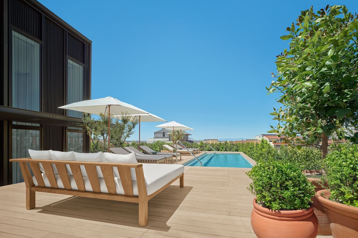 A modern outdoor pool area with a wooden deck, lounge chairs, and potted plants.