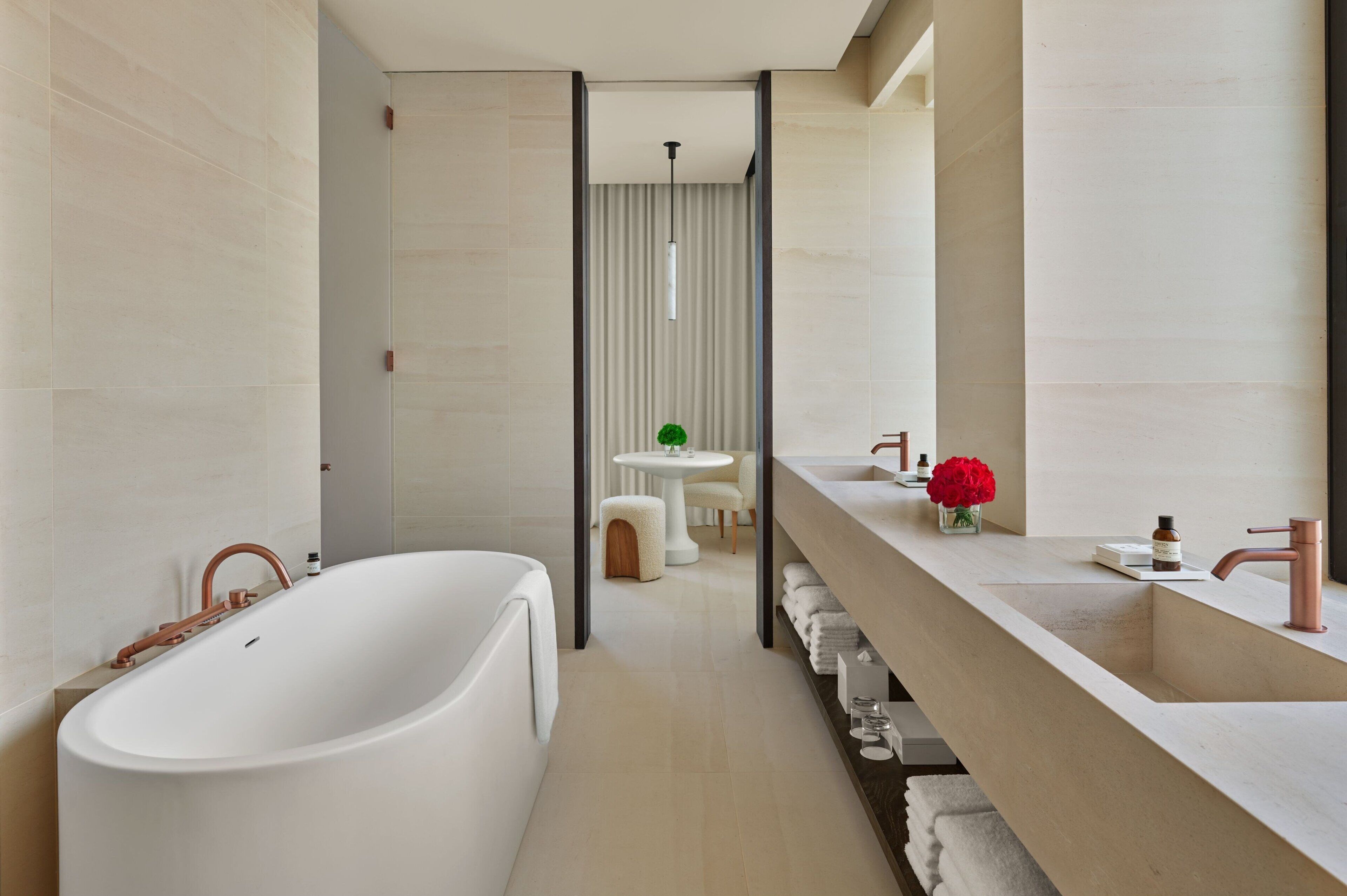 A modern bathroom with a freestanding bathtub, a large vanity with a mirror, and a small round table with a chair in the background.