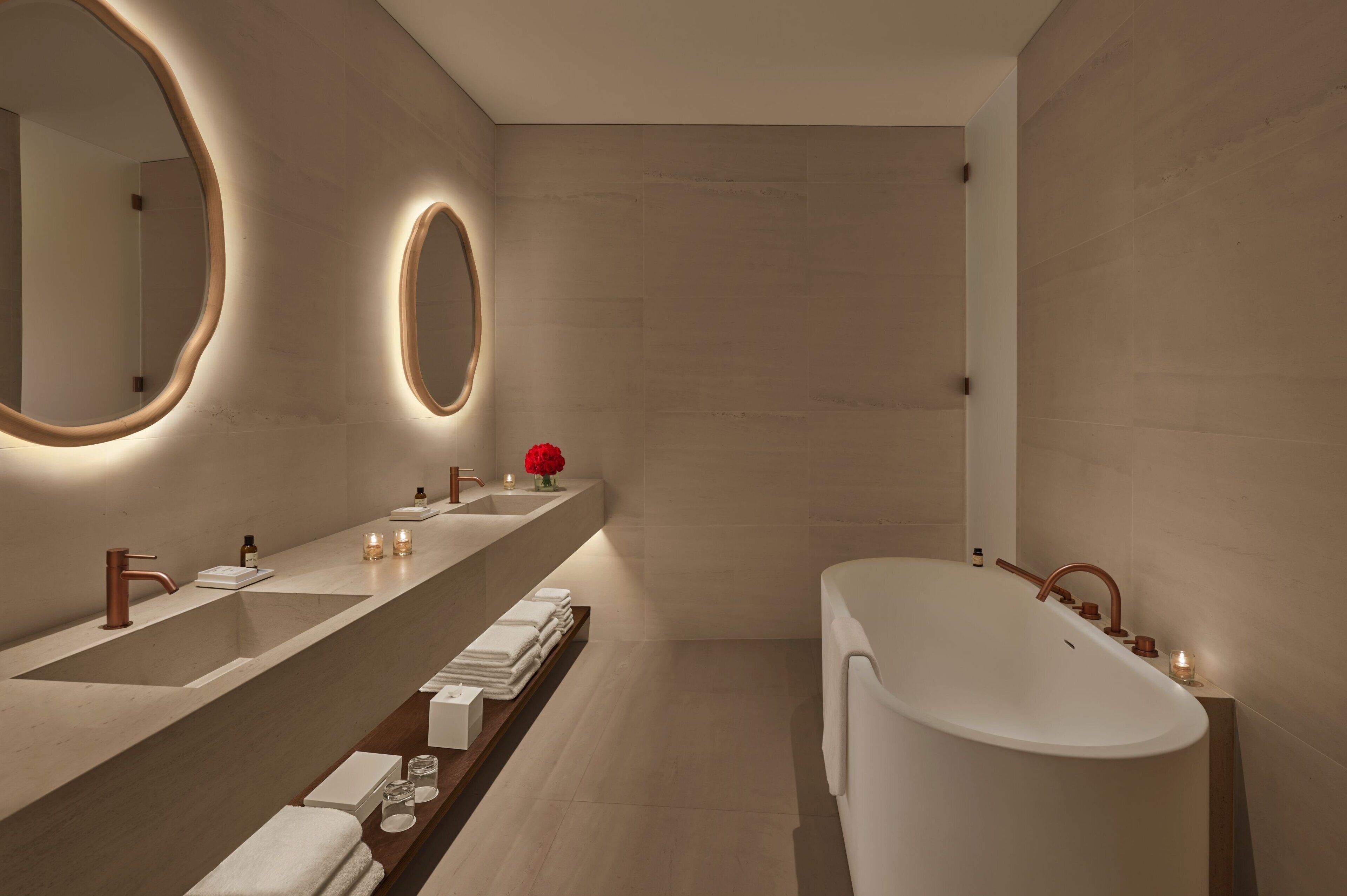 A modern bathroom with a large bathtub, a long vanity with multiple sinks, and two wall-mounted mirrors.